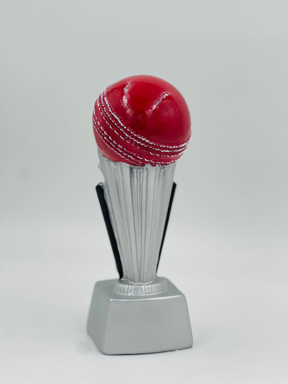 Detailed close-up of a silver-finish sports award featuring a mounted red cricket ball and a clear, flat base for personalization.