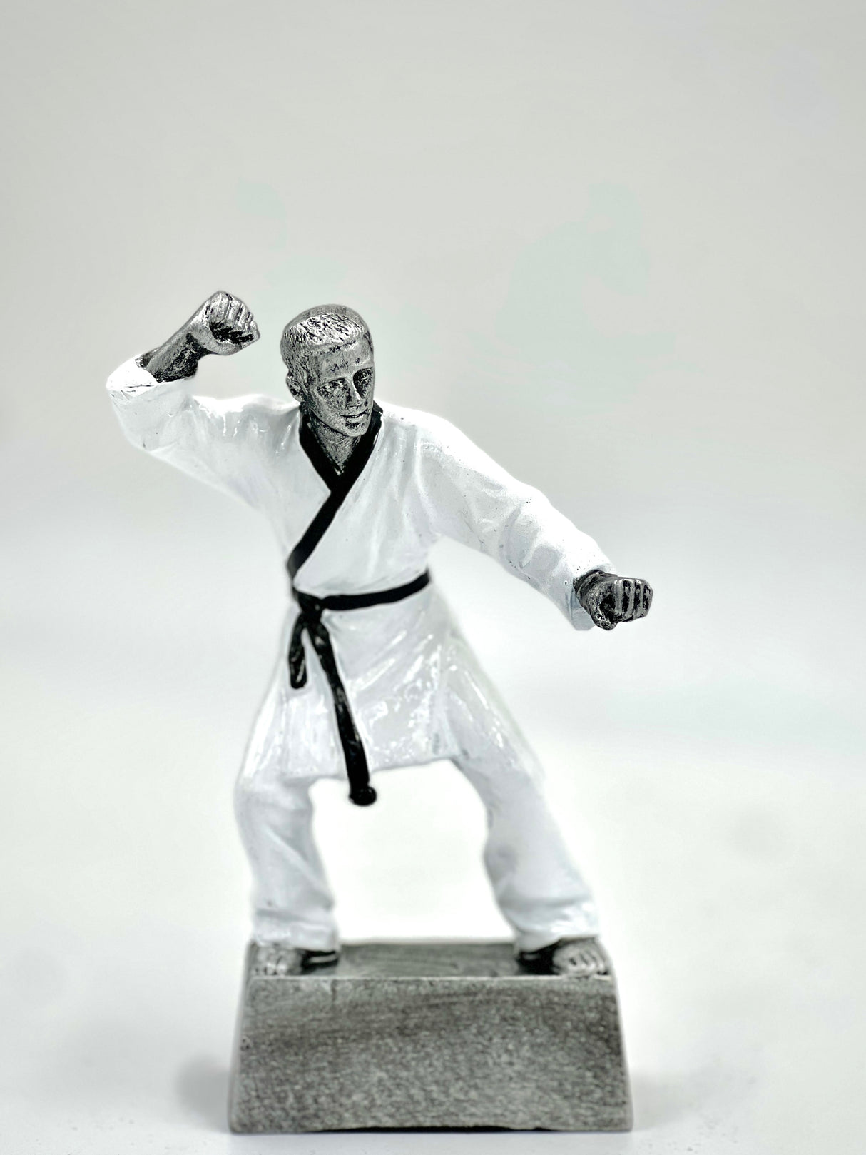 Silver martial arts trophy statue in a fighting pose with a black belt on a gray base.