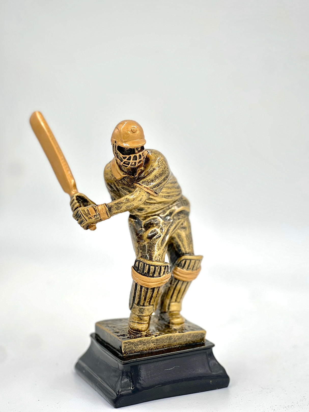 Bronze-colored cricket player statue with bat on a black base.