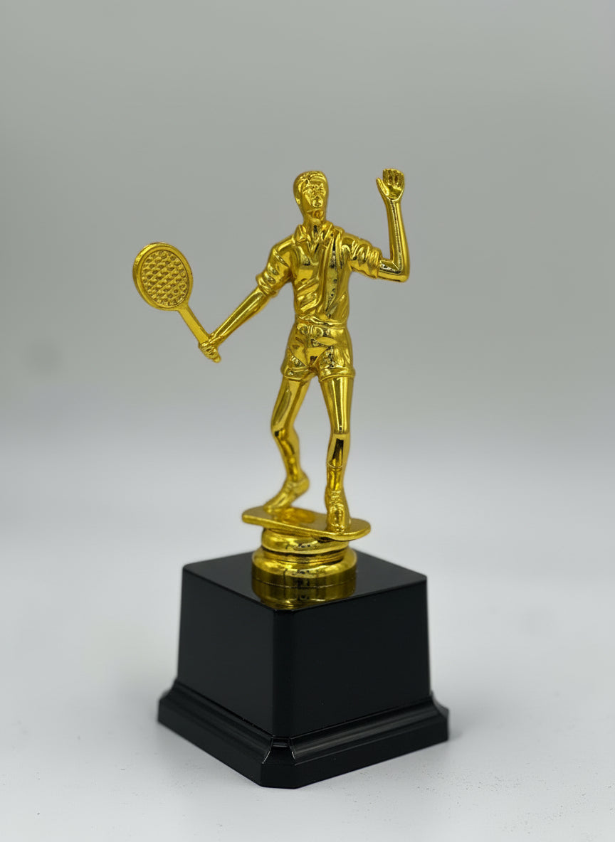 Gold tennis player figure trophy in a serving pose on a black base.