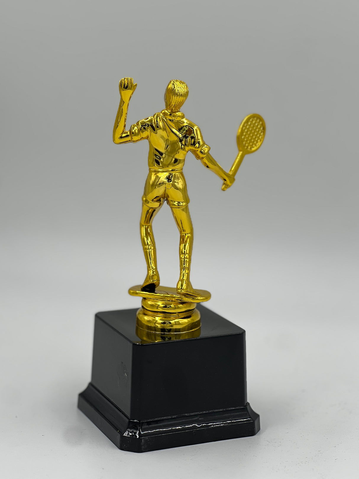 Detailed gold metallic tennis player statue with a racket, mounted on a solid black pedestal.