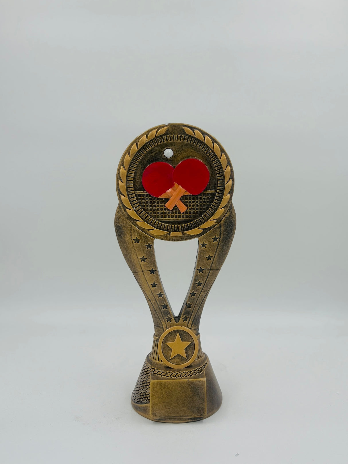 Bronze table tennis trophy award with detailed, textured base and an emblem featuring a red ping pong paddle and ball on a white background.